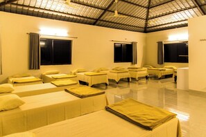 A room with multiple beds arranged in rows, a high ceiling, and large windows with curtains.