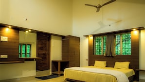 A bedroom with a bed, a ceiling fan, a window with curtains, and a mirror. - Parampara Cottages (Haliyal)