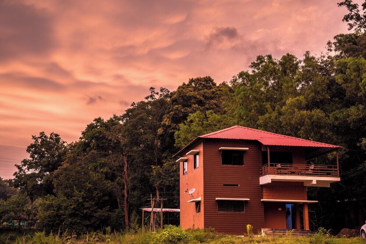 Un edificio de dos plantas con techo rojo, rodeado de un bosque denso.