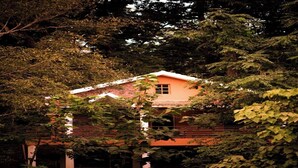 A building partially obscured by foliage, with a visible window and a brick facade. - Parampara Cottages (Haliyal)
