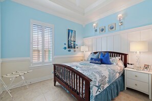 Ein Schlafzimmer mit einem Bett, einem Nachttisch, einer Lampe, einem Fenster mit Jalousien und einem Babybett.