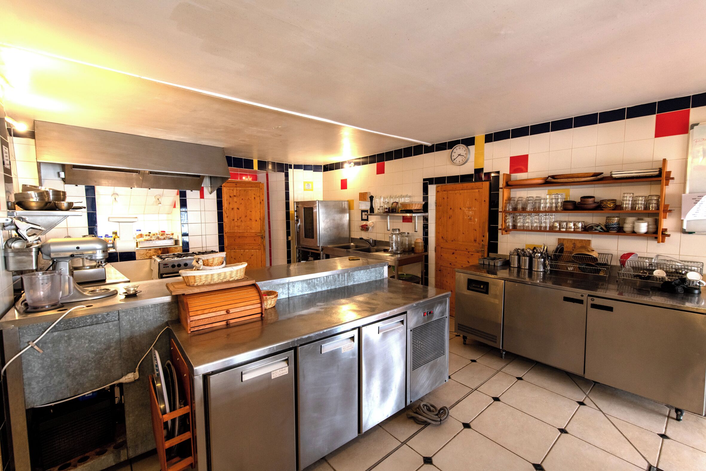 Een professionele keuken met roestvrijstalen apparatuur, een klok en betegelde muren.