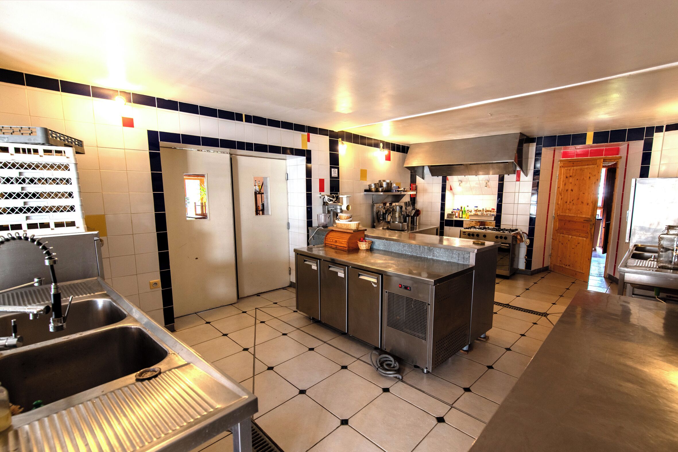 Een commerciële keuken met roestvrijstalen apparatuur, een centraal kookeiland en betegelde vloeren.