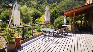 Un patio in legno con tavolo e sedie, circondato da piante in vaso e un tenda rossa.