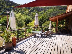 A wooden deck with a table and chairs, surrounded by potted plants and a red canopy.