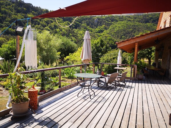 A wooden deck with a table and chairs, surrounded by potted plants and a red canopy.