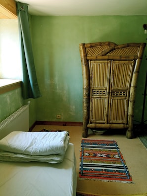 A room with a bed, a large woven chair, and a patterned rug.