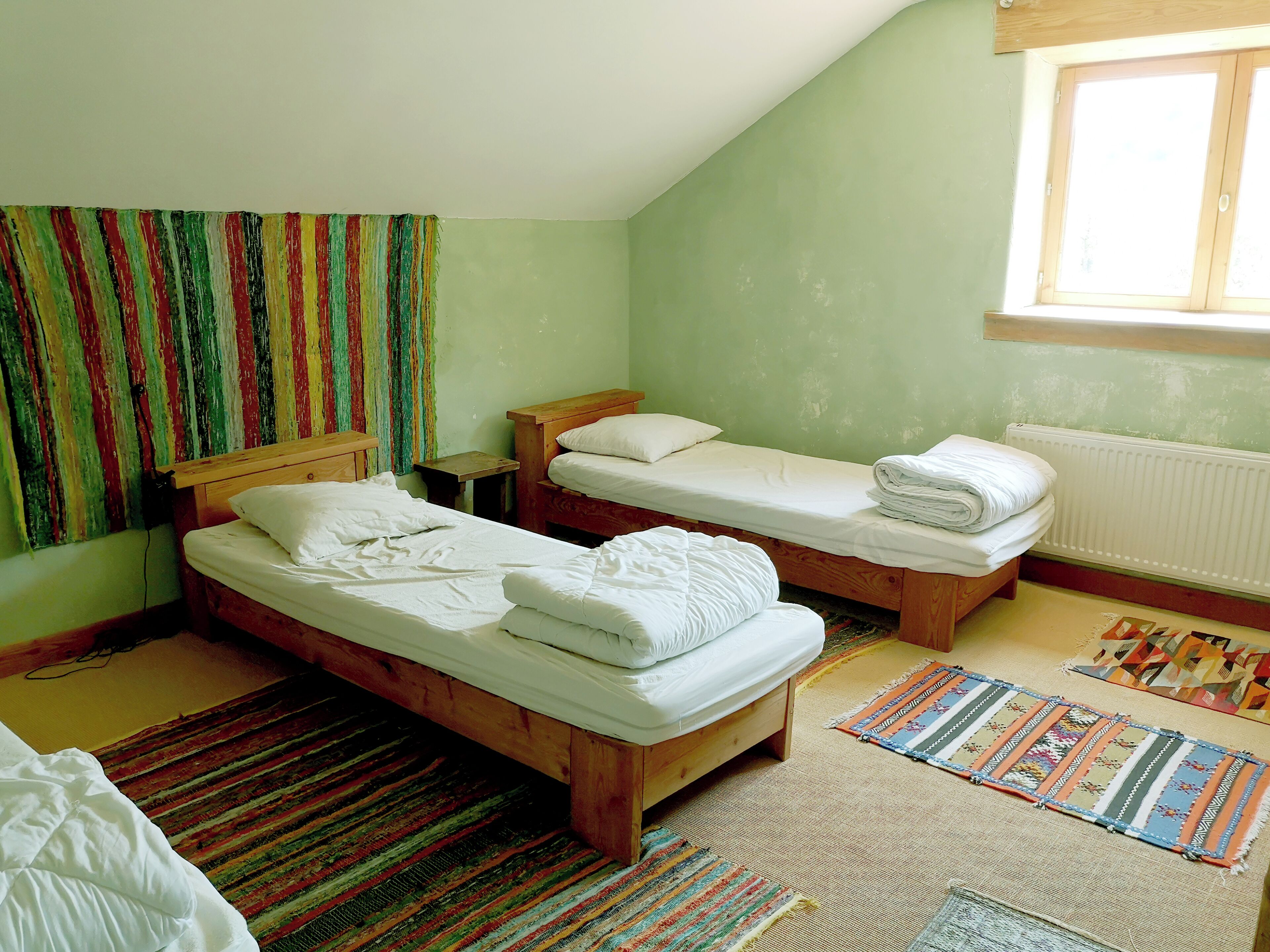 Een kamer met twee houten bedden, een tafeltje, een kleurrijk gestreept tapijt en een raam met uitzicht.