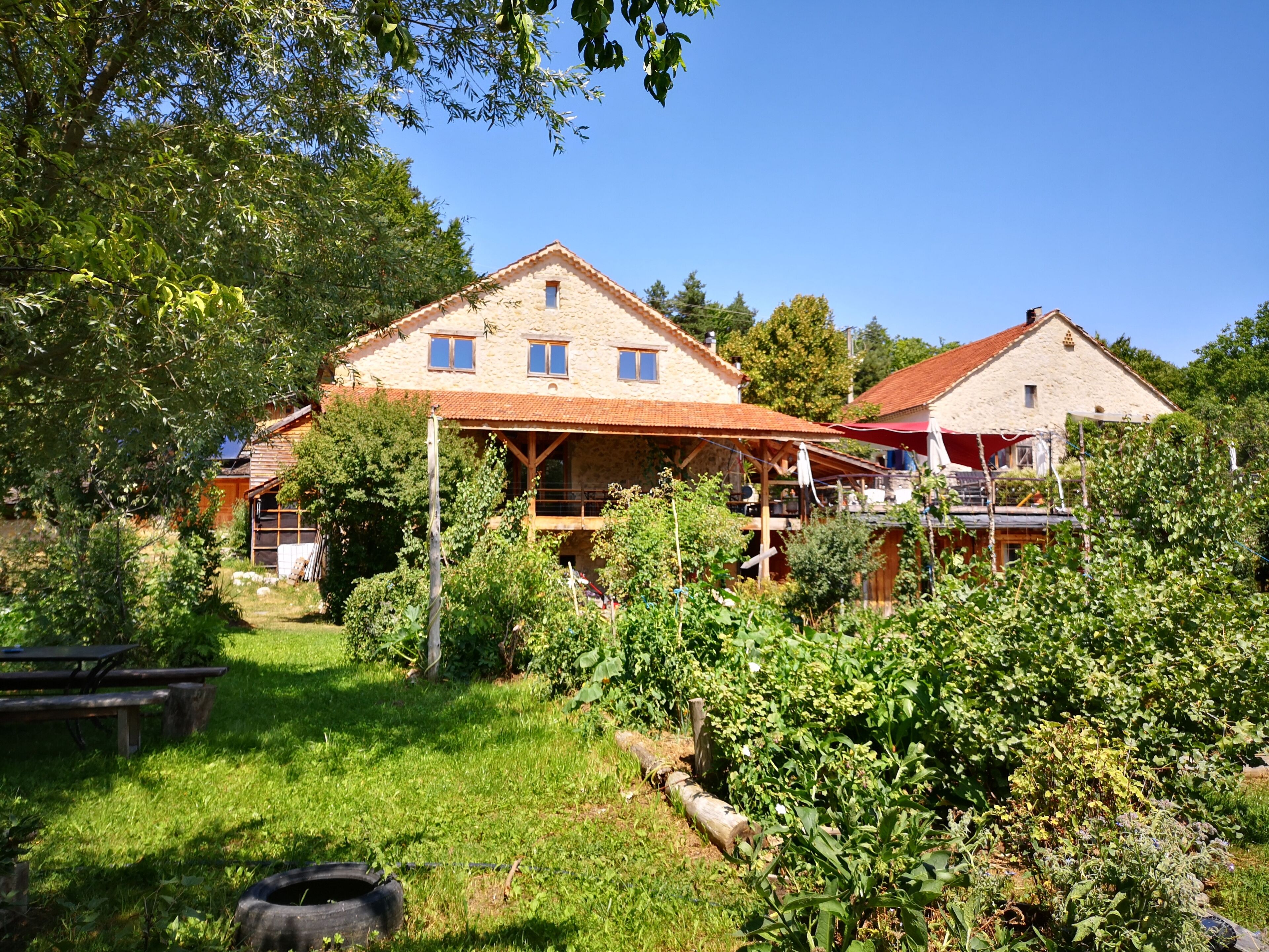 A stone building with a red roof, surrounded by greenery and a picnic table.