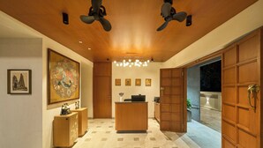 A hotel lobby with a reception desk, a large painting, and a ceiling fan.