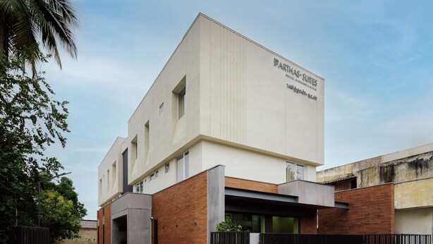 A modern building with a flat roof, a sign reading 'PARTHAS SUITES,' and a gated entrance.