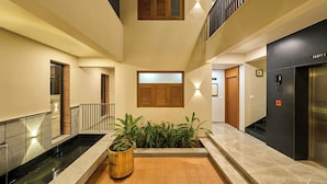 A hotel lobby with a central water feature, a reception desk, and a staircase leading to an upper level. - Parthas suites (Tiruchirappalli)