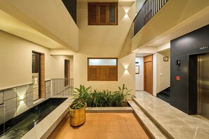 A hotel lobby with a central water feature, a reception desk, and a staircase leading to an upper level.
