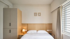A hotel room with a bed, bedside tables, a wardrobe, and a window with curtains. - Parthas suites (Tiruchirappalli)