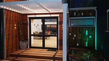 A modern house with a covered entrance, a dining area visible through glass doors, and a garden with plants.