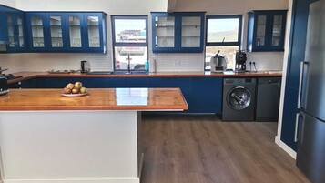 A modern kitchen with blue cabinets, a wooden countertop, and a built-in washing machine.