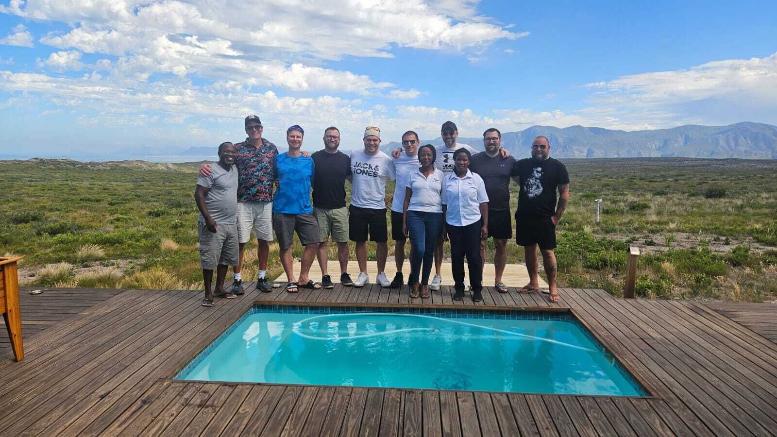 A group of people standing on a wooden deck with a pool in the foreground.