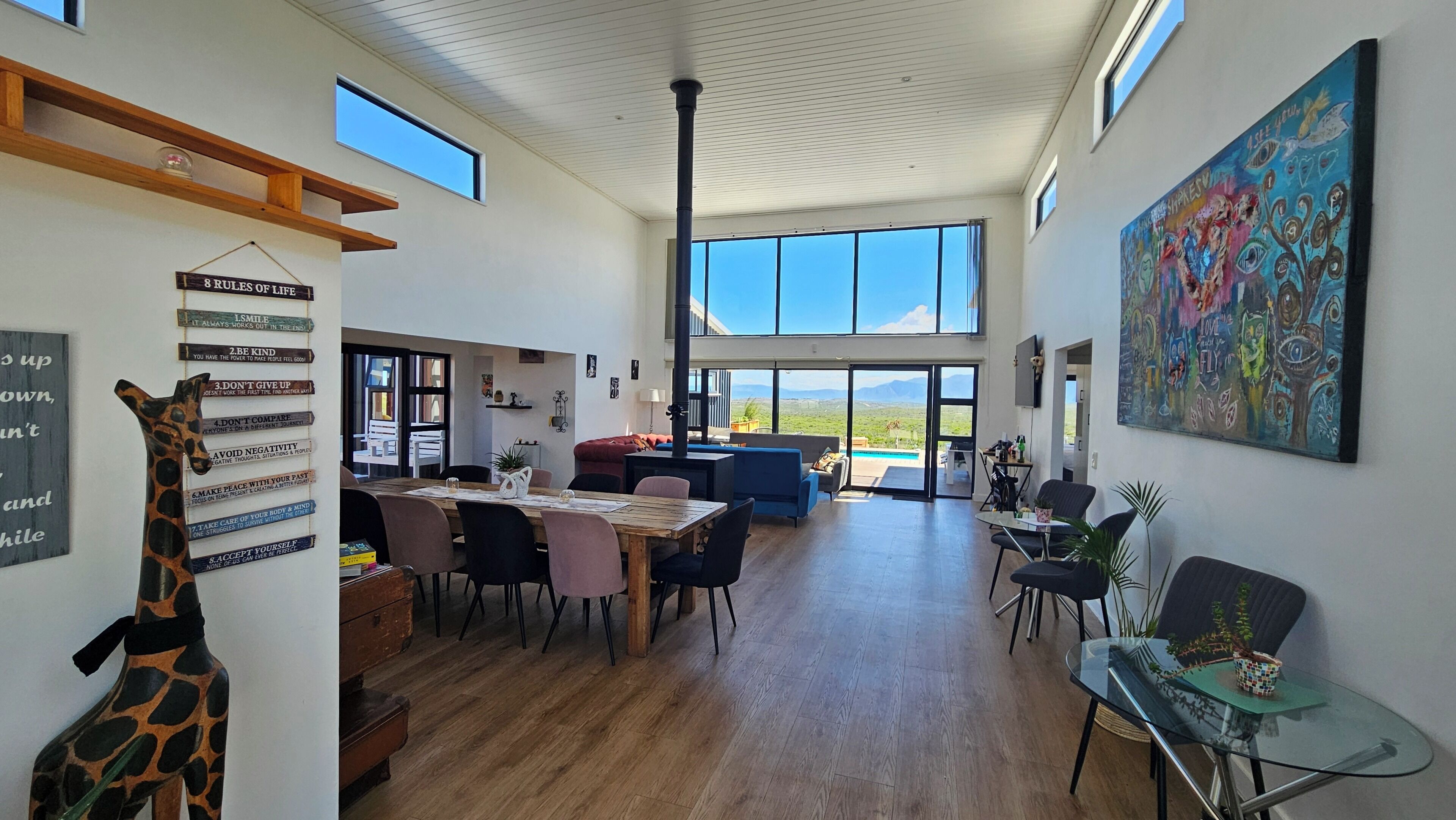 A spacious living area with a high ceiling, large windows, and a dining area with a wooden table and chairs.