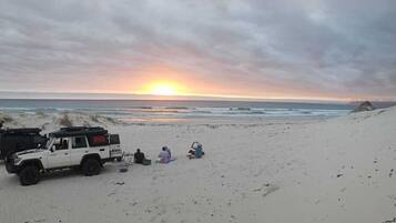 A beach with a sunset, a dune buggy, and people relaxing.