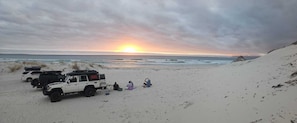 A beach with a sunset, a dune buggy, and people relaxing.