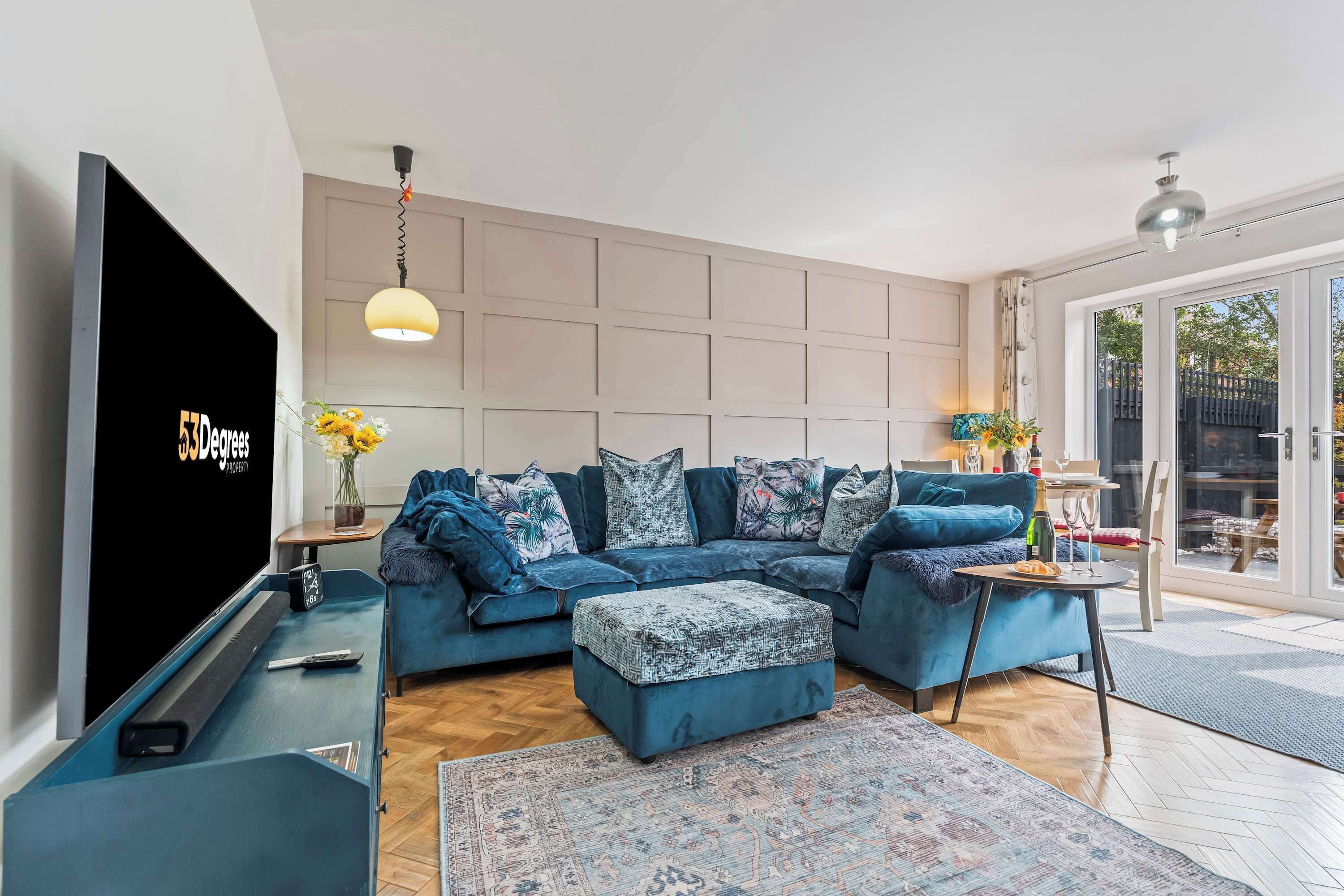 Un salon moderne avec un canapé d’angle, un téléviseur à écran plat, une petite table et une grande fenêtre.