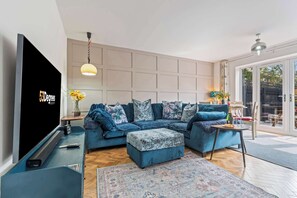 Ein modernes Wohnzimmer mit einem Ecksofa, einem Flachbildfernseher, einem kleinen Tisch und einem großen Fenster.