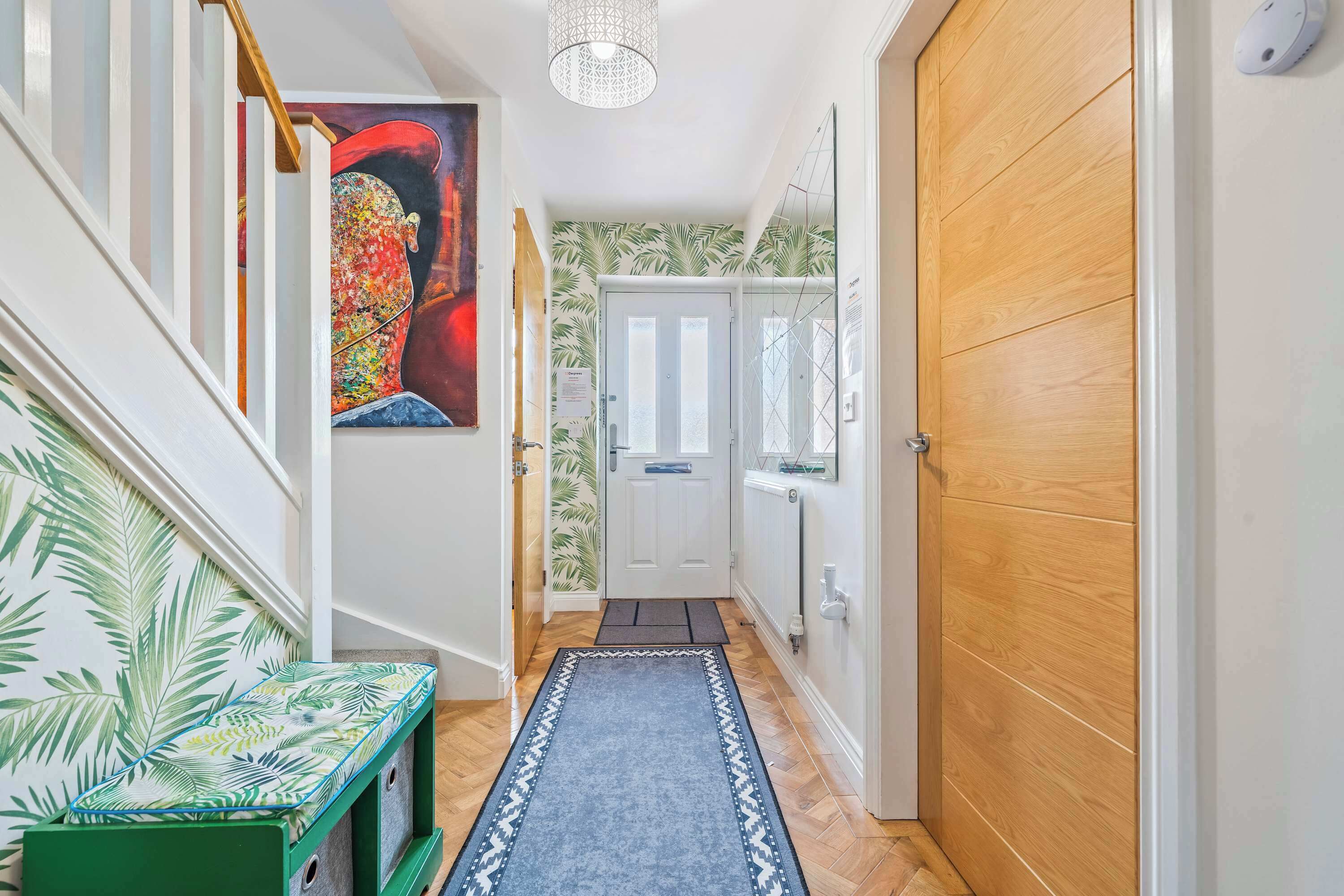 A hallway with a wooden door, a white door, a green bench, and a patterned rug.