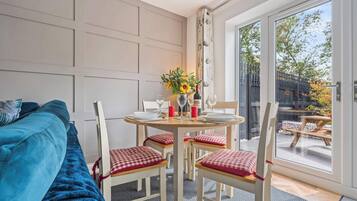 A room with a bed, a dining table set for two, and a view through a glass door to an outdoor patio.