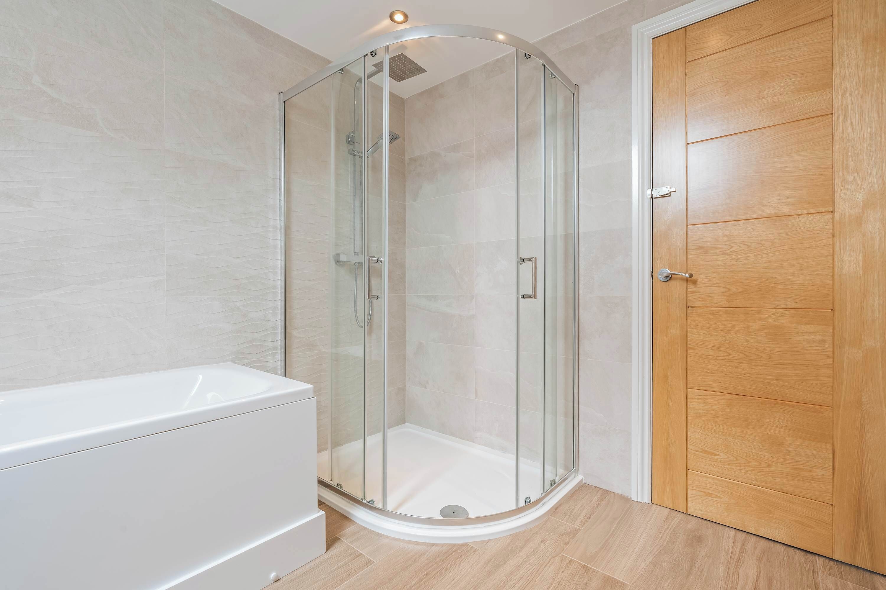 A modern bathroom with a glass-enclosed shower, a white bathtub, and a wooden door.