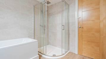 A modern bathroom with a glass-enclosed shower, a white bathtub, and a wooden door.
