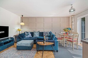 Ein modernes Wohnzimmer mit einem Ecksofa, einem Couchtisch, einem Fernseher und einem Essbereich mit Tisch und Stühlen.