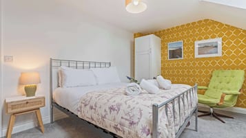 A bedroom with a bed, a nightstand, a lamp, a wardrobe, a chair, and two framed pictures on the wall.
