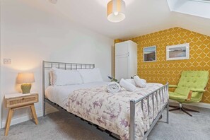 Ein Schlafzimmer mit einem Bett, einem Nachttisch, einer Lampe, einem Kleiderschrank, einem Sessel und zwei gerahmten Bildern an der Wand.