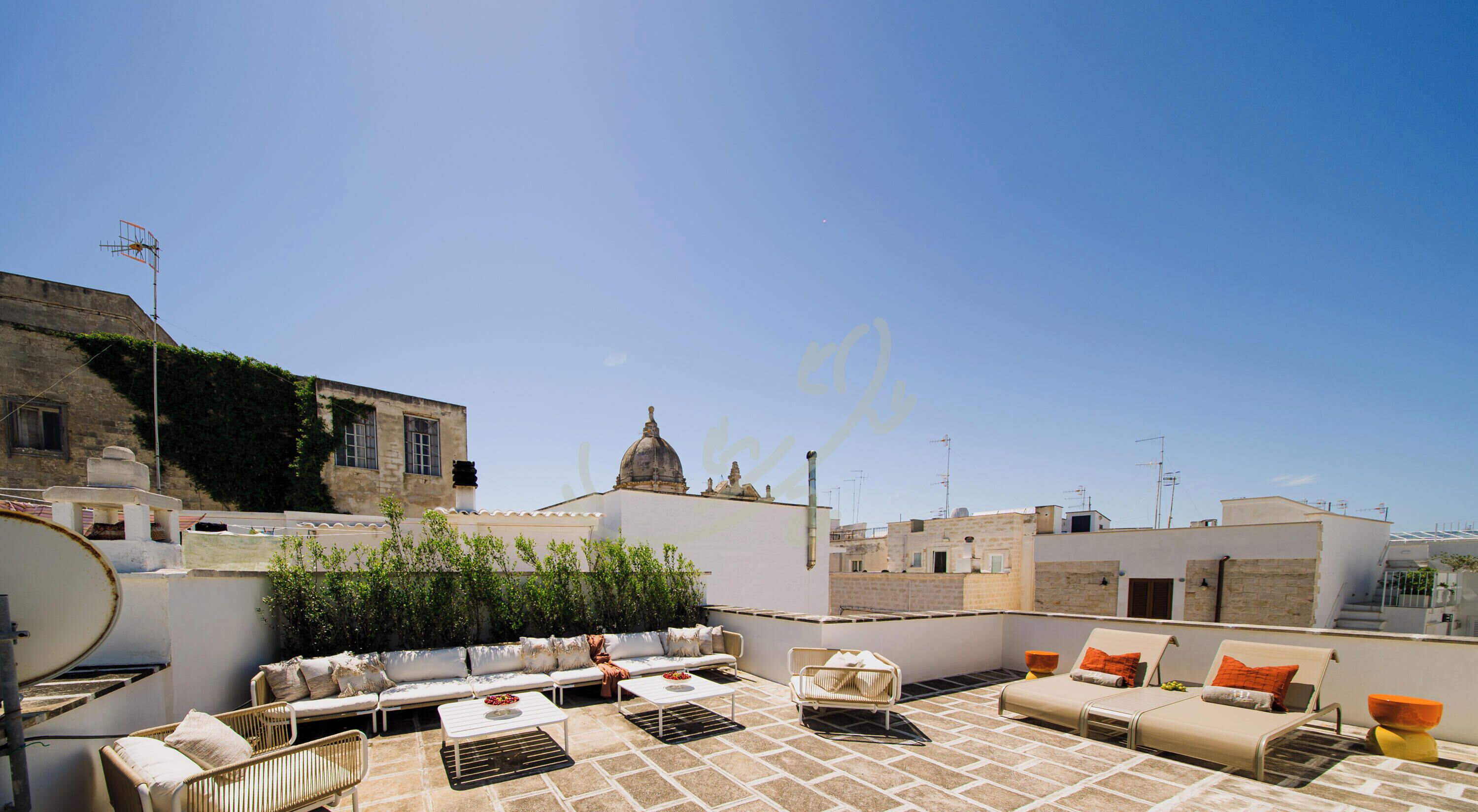 Eine Dachterrasse mit Sitzgelegenheiten im Freien, einer Satellitenschüssel und Blick auf die Stadtlandschaft.