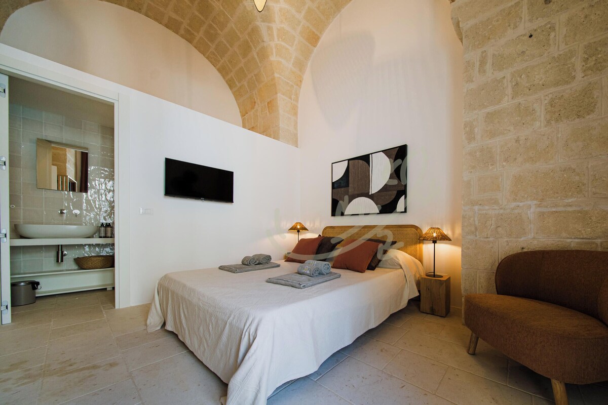 Ein Schlafzimmer mit einem Bett, zwei Nachttischlampen, einem Fernseher und einer Steinwand.