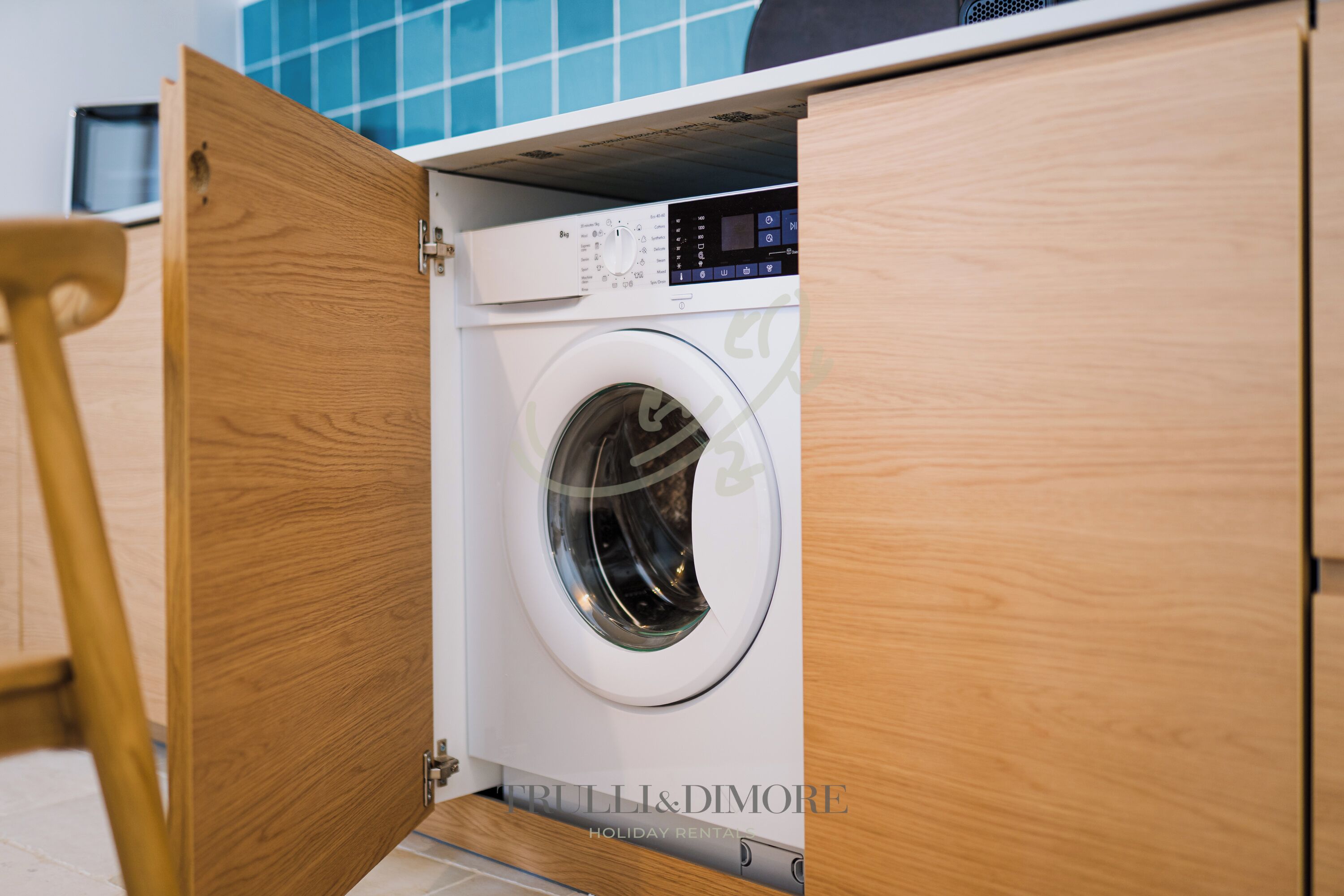 A front-loading washing machine in a wooden cabinet with a digital control panel.