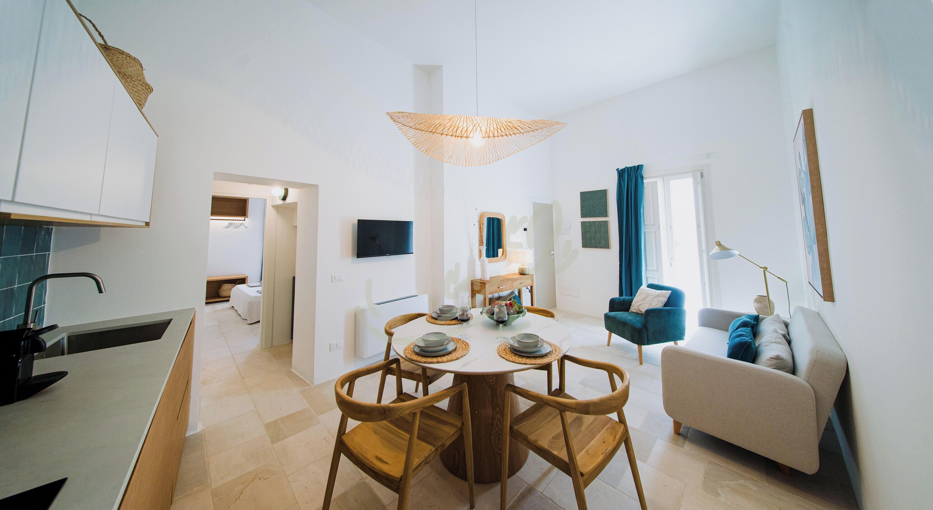 Uma sala de estar moderna com uma mesa de jantar redonda, cadeiras de madeira, um sofá e uma TV fixada na parede.