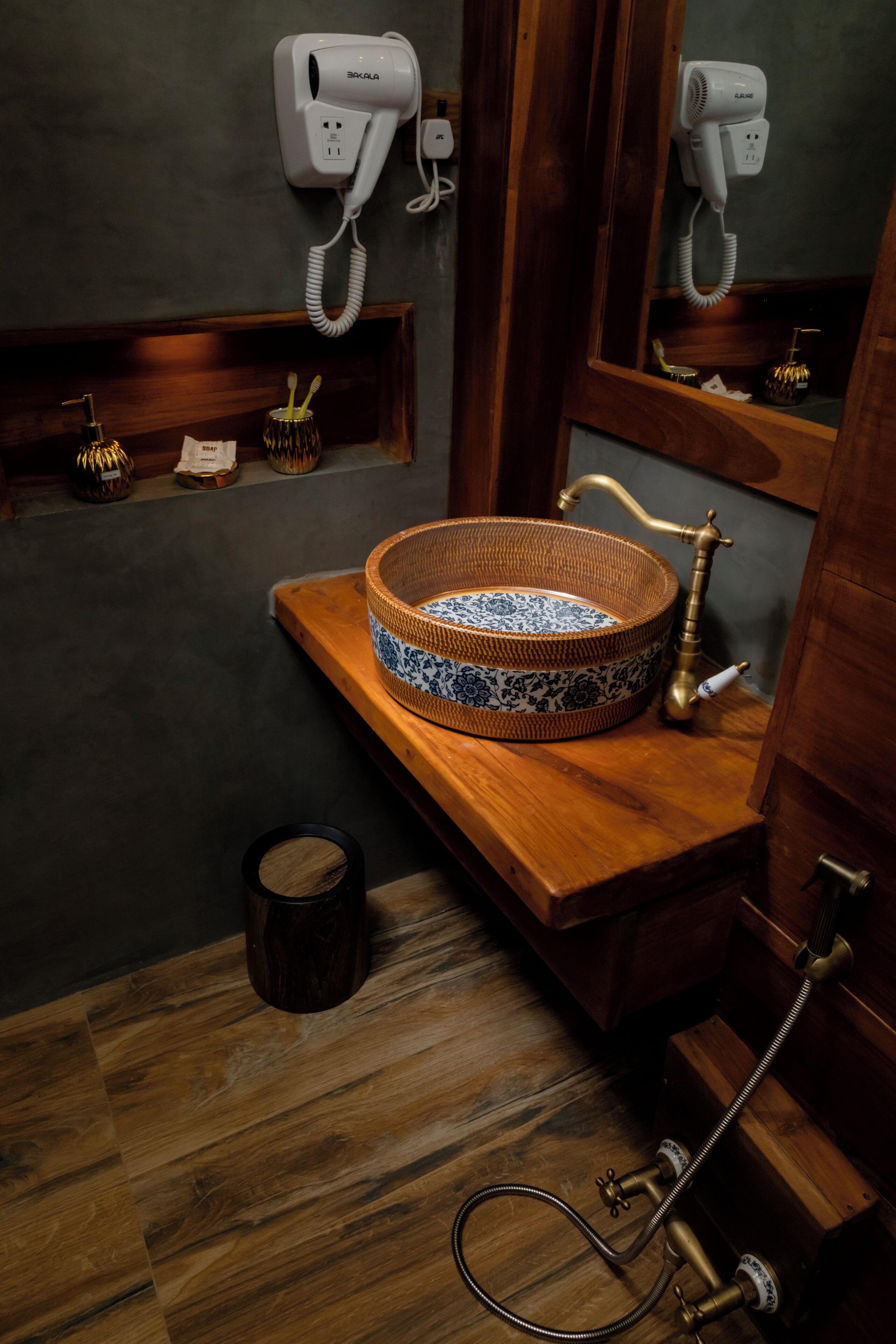 A bathroom with a wooden vanity, a sink with a decorative bowl, a mirror, and a hairdryer mounted on the wall.