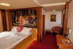 A hotel room with a large bed, a painting on the wall, a small table, and a chair.