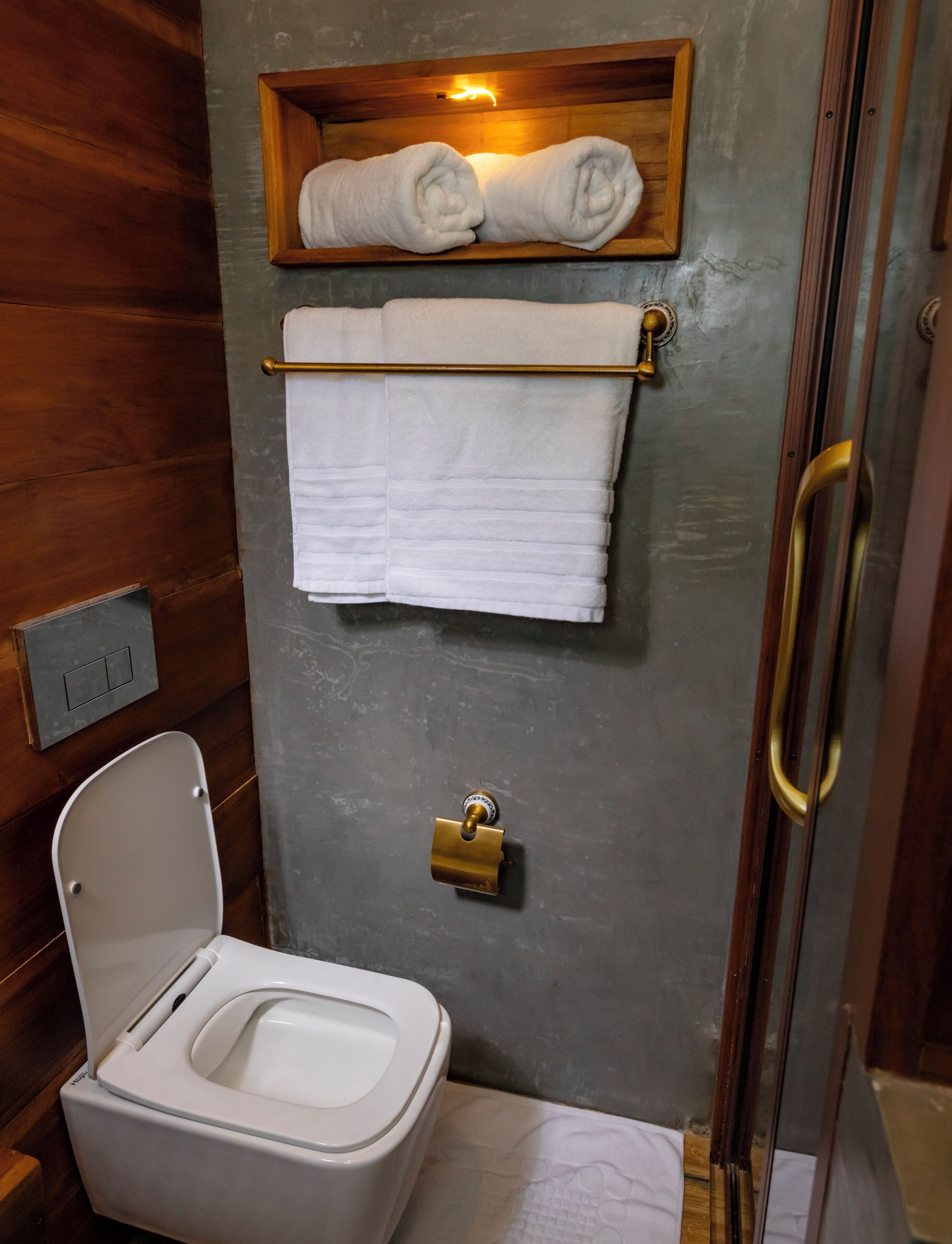 Een kleine badkamer met toilet, een handdoekrek met opgevouwen handdoeken, en een slot op de deur.