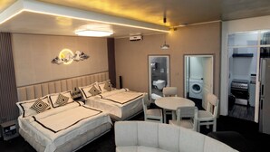 Une chambre d’hôtel avec deux lits, un coin salon, un lavabo et une petite kitchenette.