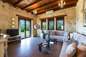 A spacious living room with stone walls, a wooden ceiling, a television, a sofa, and a coffee table. - Poseidon, Authentic Cretan Stone Villa, Private Pool, Refined Spaces, Warm Charm (Lefkogia)
