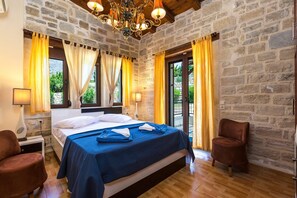 A bedroom with a stone wall, a bed with a blue bedspread, two chairs, and a chandelier. - Poseidon, Authentic Cretan Stone Villa, Private Pool, Refined Spaces, Warm Charm (Lefkogia)