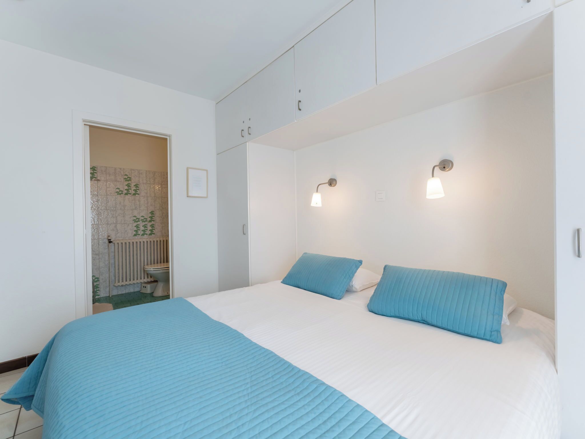 Een slaapkamer met een bed, twee bedlampen, een deur naar een badkamer, en een gecertificeerde oorkonde aan de muur.