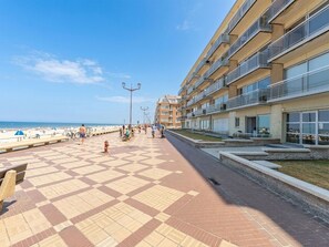 Eine Strandpromenade mit Schachbrettmuster-Bodenbelag, einem Hydranten und einer Reihe mehrstöckiger Gebäude mit Balkonen.