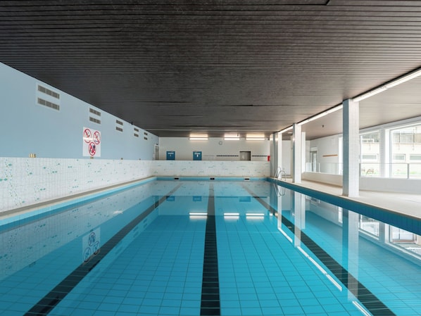 Ein Innenpool mit hellblauen Fliesen, einem gefliesten Boden und einer Decke mit linearem Muster.