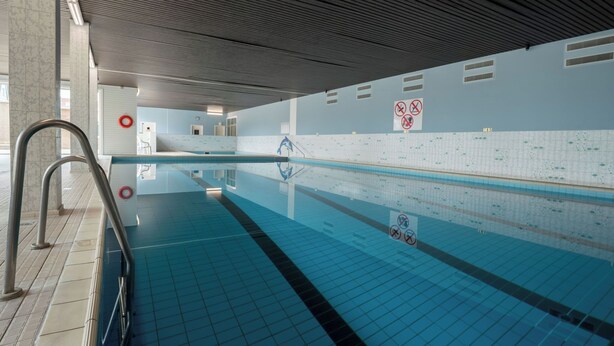 Une piscine intérieure aux murs recouverts de carreaux, à l’eau claire et au plafond orné de motifs en relief.