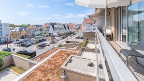 Un balcon avec un parasol blanc, une vue sur un parking et des bâtiments en arrière-plan.