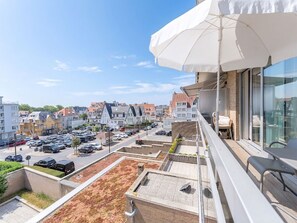 A balcony with a white umbrella, a view of a parking lot, and buildings in the background.