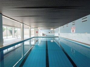 Una piscina interior amb línies delimitades, terra de rajola i sostre ventilat.